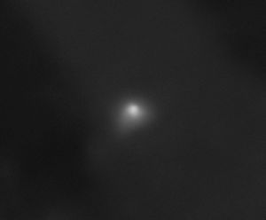 On a largely black background, interstellar comet 3I/ATLAS appears as a white smudge with a semicircular shape at its core. A transparent white cloud extends slightly from the comet toward the bottom left of the image and, to a lesser extent, toward the right side of the image